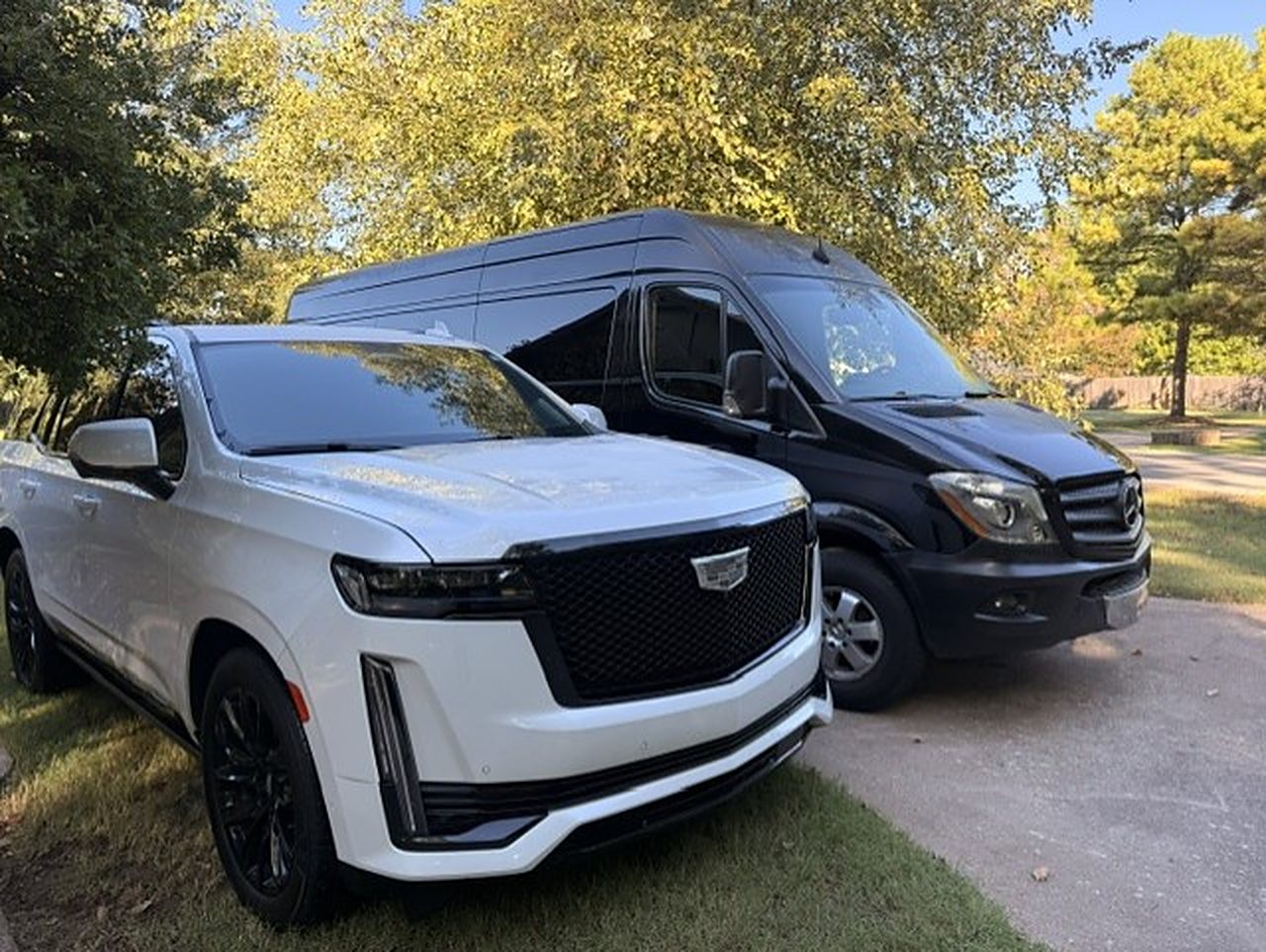 White Cadillac Escalade parked beside the black Mercedes Sprinter