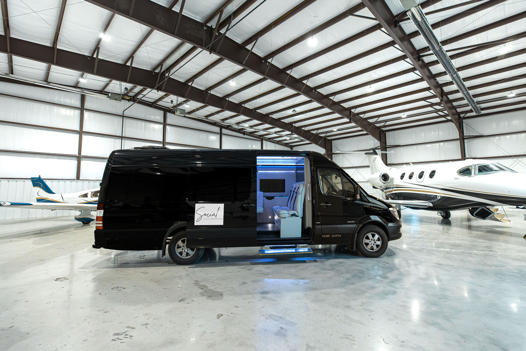 Black luxury Mercedes Sprinter parked beside private jets in a Tulsa hangar