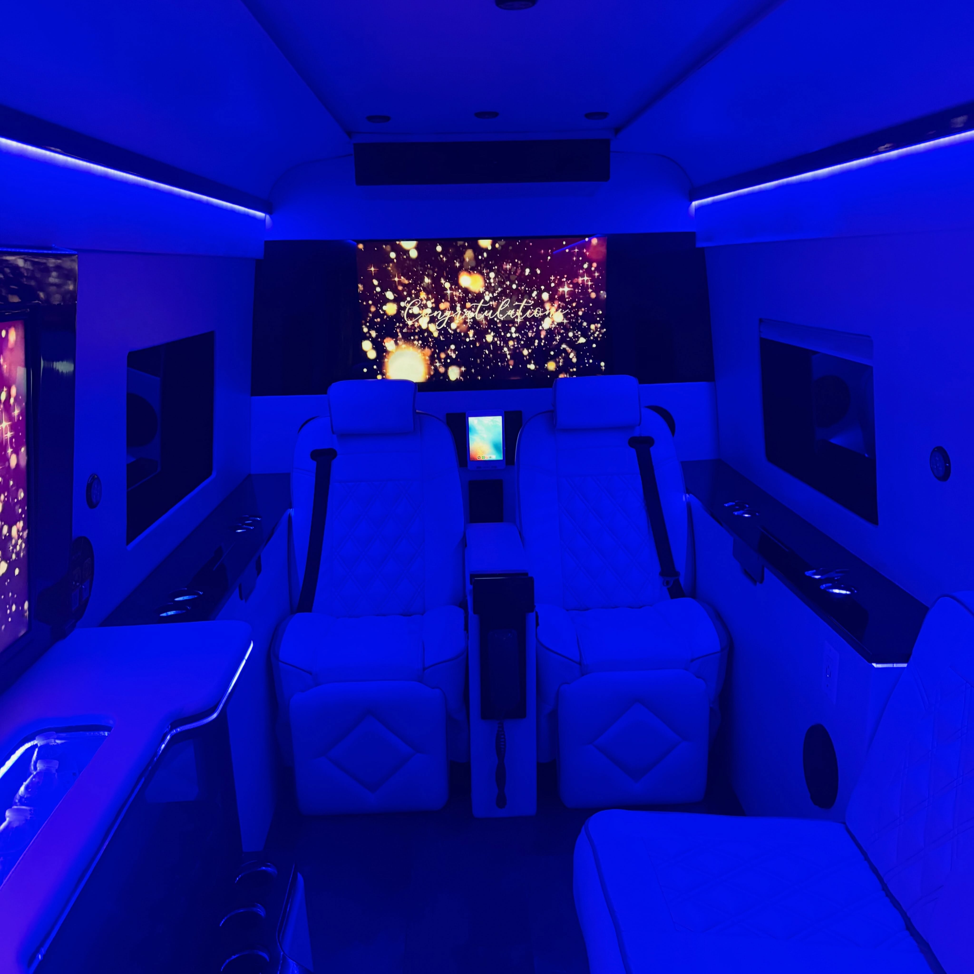Luxury van interior with white leather seats, blue LED lighting and a screen showing gold sparkles and a Congratulations message