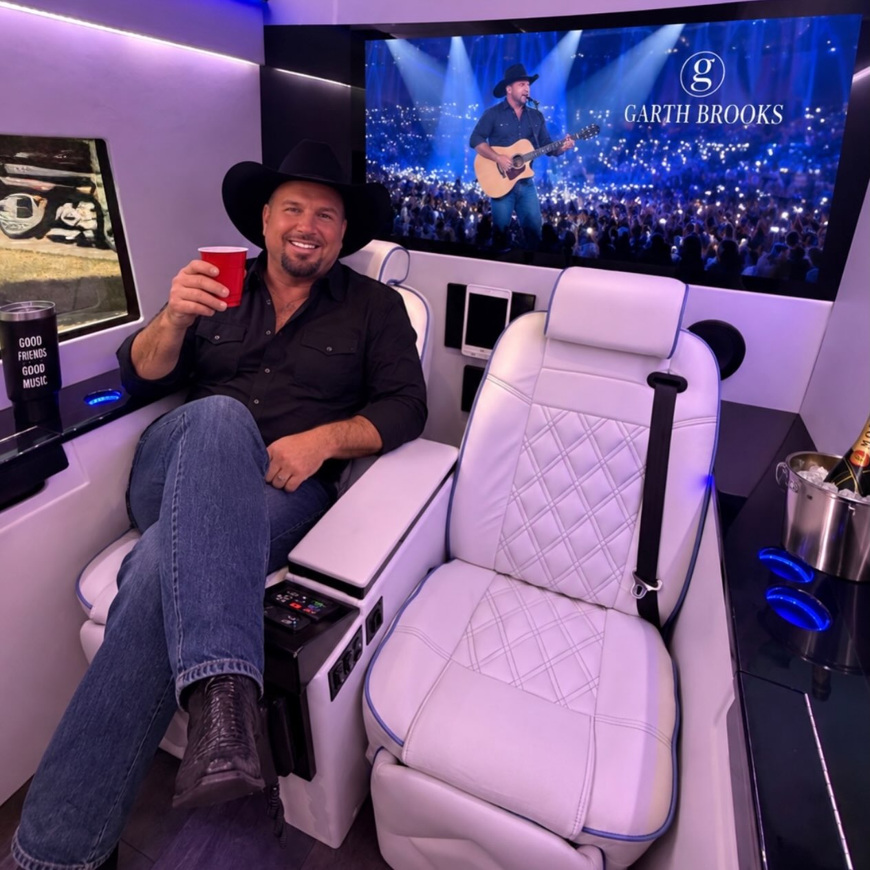 Man in black cowboy hat holding red cup relaxes in white quilted leather luxury van seat with large screen behind him